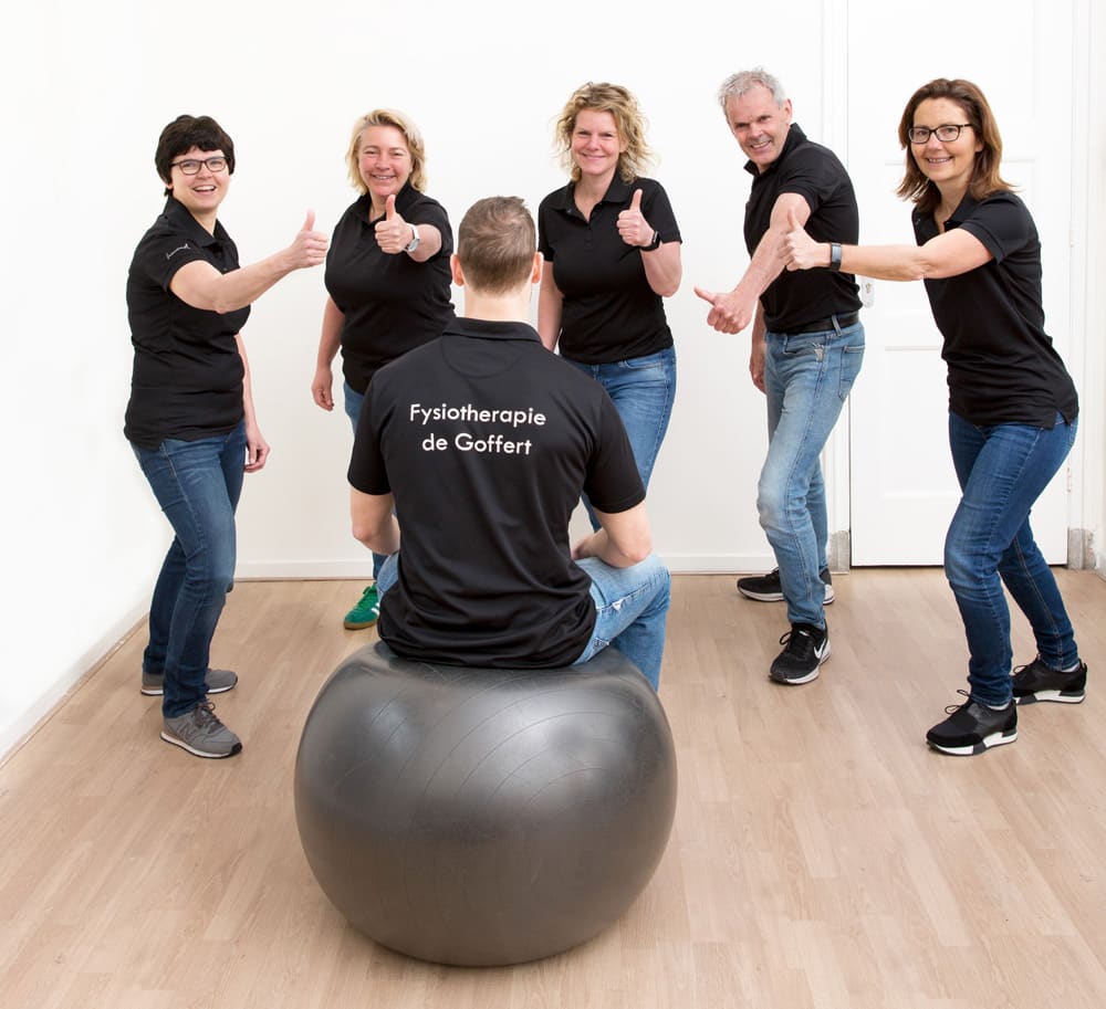 Zes medewerkers van Fysiotherapie de Goffert steken hun duim op rond een collega op een oefenbal